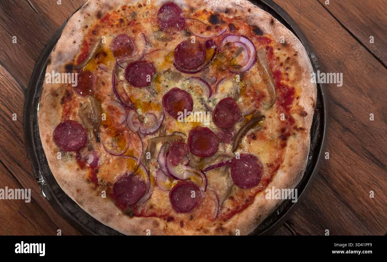 Pizza piccante con salsiccia con cipolla rossa e formaggio fuso su un tavolo di legno Foto Stock