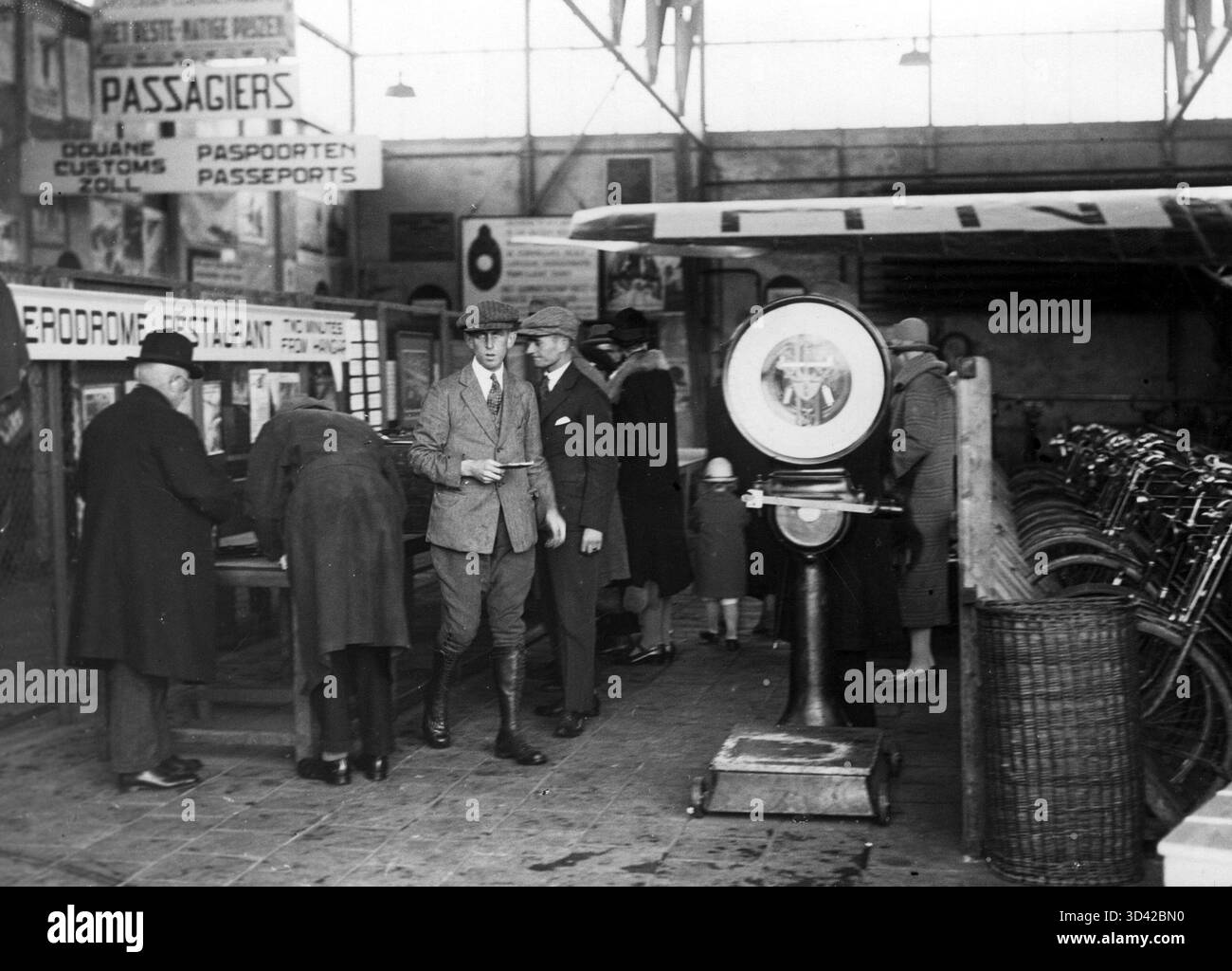 I passeggeri sono visibili nella sala dell'aeroporto di Schiphol, con un ristorante, un deposito biciclette e un'area doganale nelle vicinanze. La foto cattura l'aviazione dei primi anni del XX secolo a Schiphol, Paesi Bassi, intorno al 1927. Foto Stock