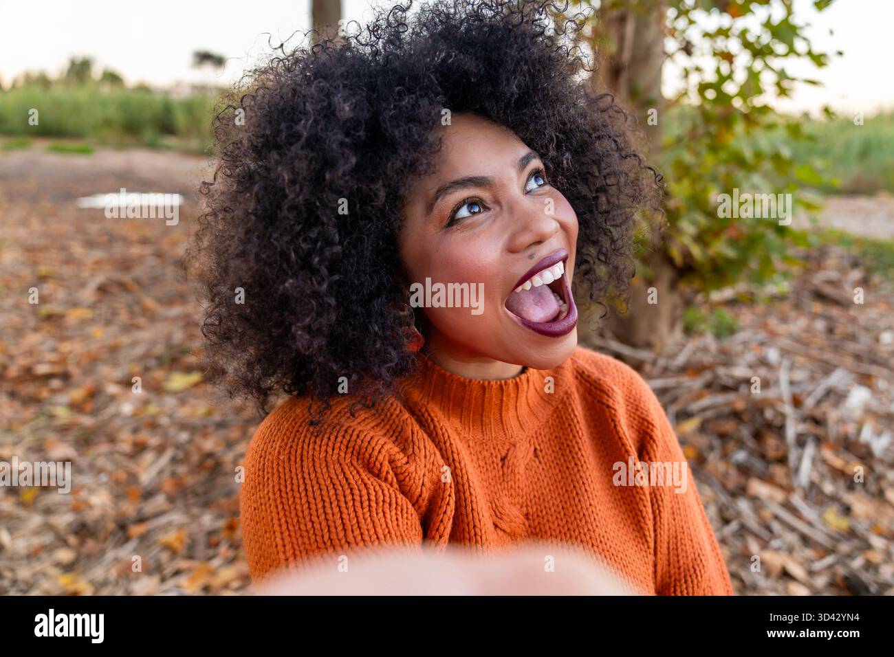 Giovane donna felice con capelli ricci che guarda verso l'alto con un'espressione eccitata e a bocca aperta Foto Stock