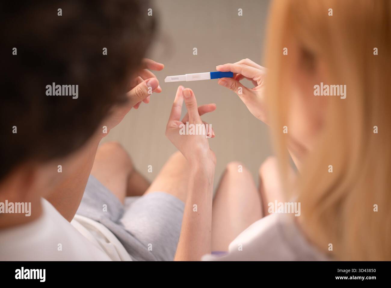 Coppia felice seduta sul letto e sorridente di eccitazione guardando un test di gravidanza positivo || modello rilasciato Foto Stock