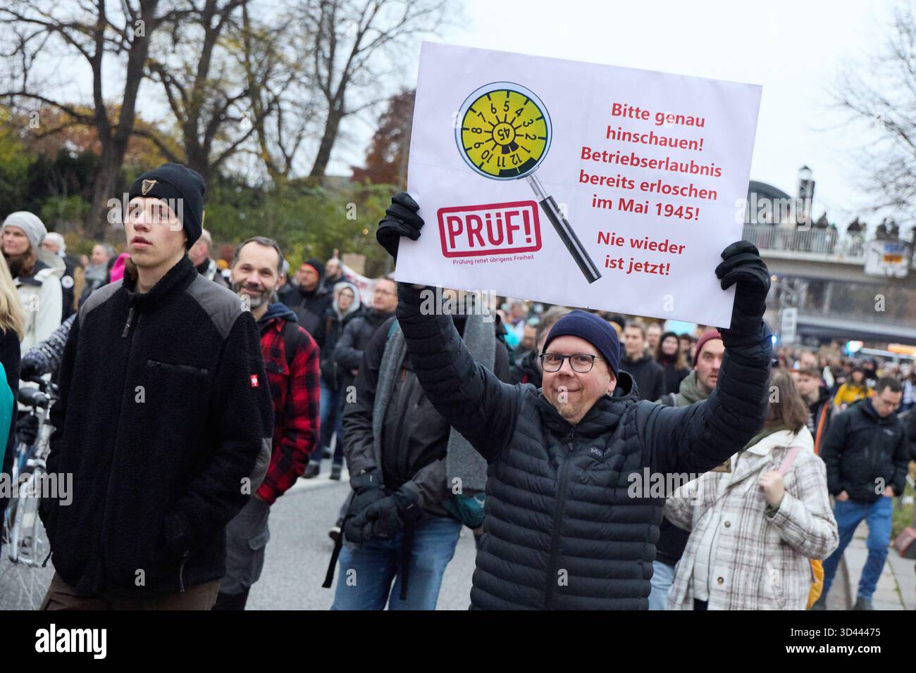Amburgo, Germania. 8 novembre 2025. Un partecipante all'evento di calcio nazionale "l'ordine deve essere: Partiti estremisti di destra alla legge fondamentale "TÜV”!” Ha un cartello sul Dammtordamm con l'iscrizione "per favore guarda! La licenza per operare è già scaduta a maggio 1945! Mai più adesso!". La campagna nazionale avviata da Prüf.de chiede che tutte le parti classificate dall'Ufficio per la protezione della Costituzione come estremisti di destra sospettati o confermati siano esaminate dalla Corte costituzionale federale. Crediti: Georg Wendt/dpa/Alamy Live News Foto Stock
