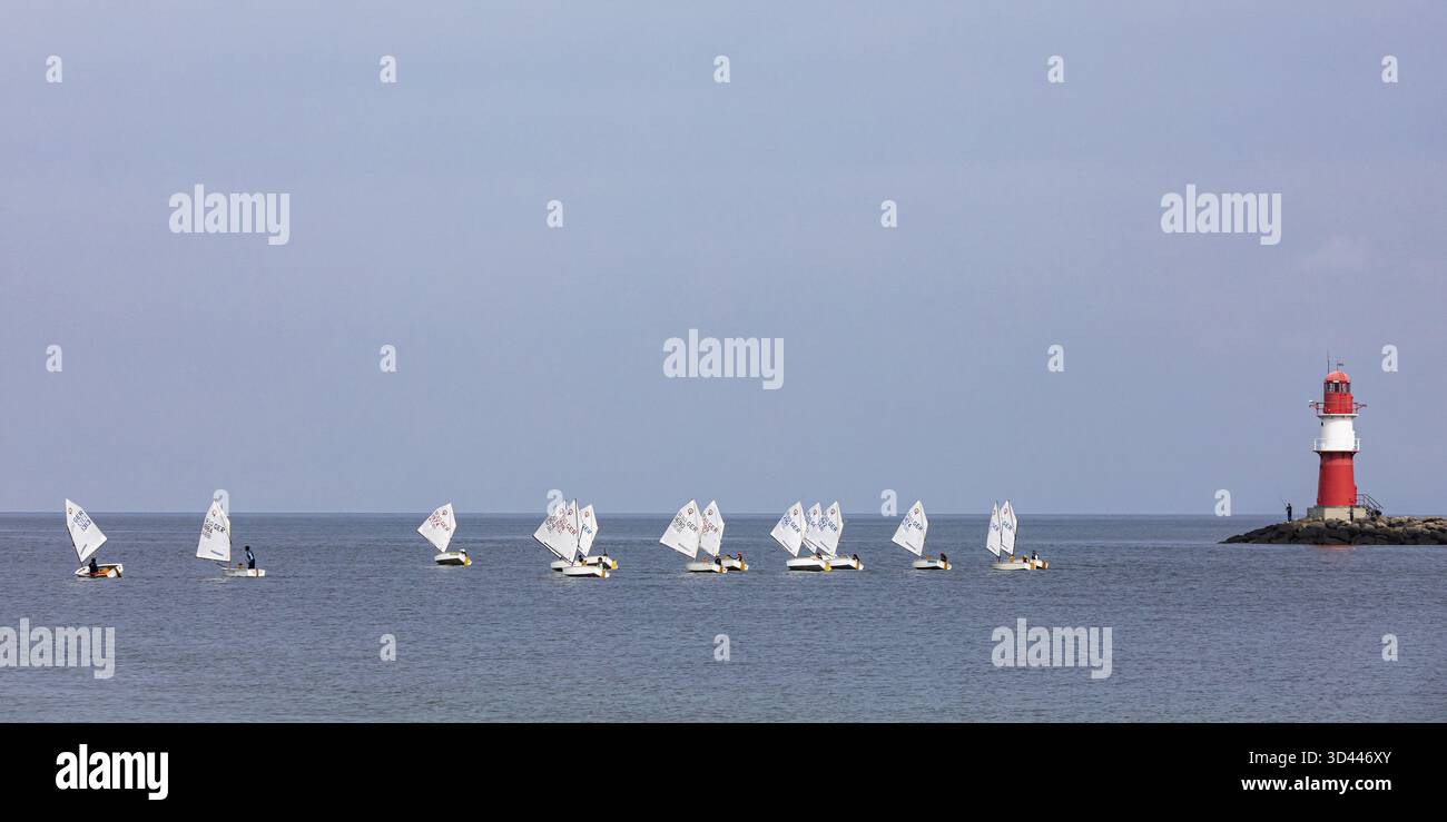 Corso di vela con barche a vela di classe Optimist, un gommone a vela e il fuoco del molo a Warnemuende, Mar Baltico, Meclemburgo-Pomerania Occidentale, Germania Foto Stock
