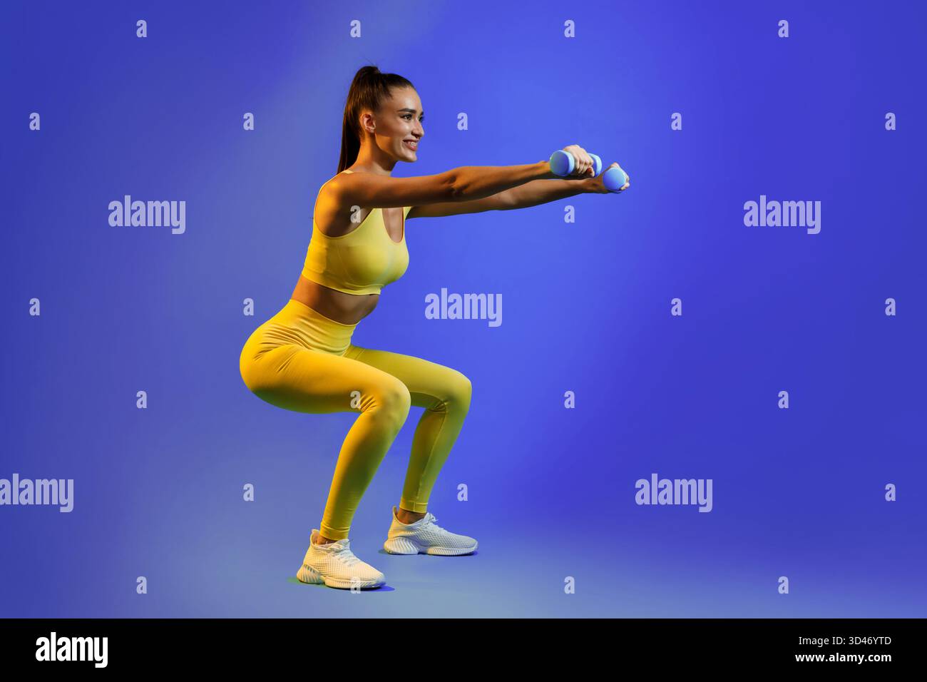 Gli appassionati di fitness eseguono squat con pesi in un abbigliamento da allenamento luminoso su sfondo blu Foto Stock