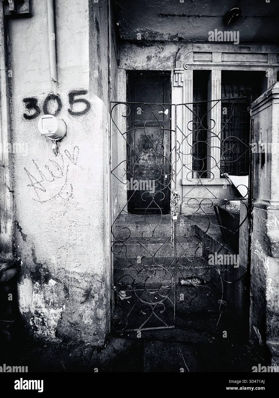 Immagine in bianco e nero di un vecchio ingresso con cancello metallico, scale e muro marcato di un edificio urbano deteriorato Foto Stock