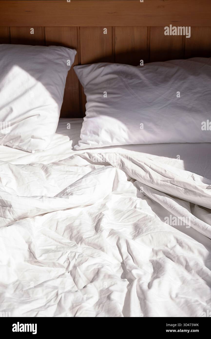 Letto non fatto con biancheria bianca alla luce del sole. Accogliente scena mattutina. Interni puliti per un concetto di relax. Foto Stock