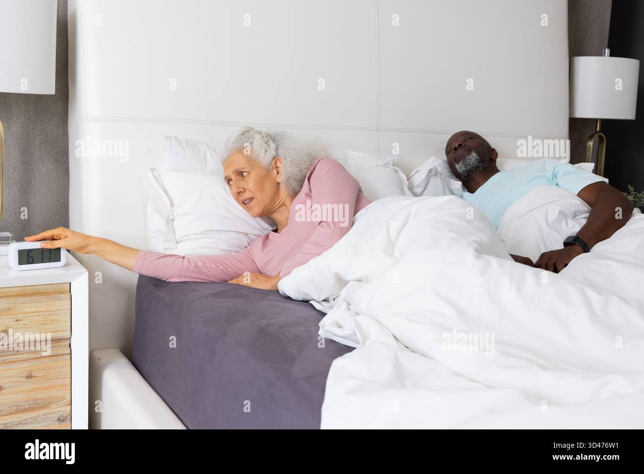 Diverse coppie anziane che si avvicinano alla sveglia mentre riposano nella camera da letto principale, con impianto Foto Stock
