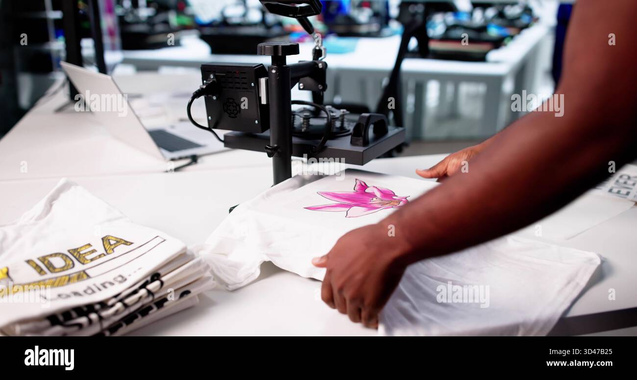 Young Black Man Operating Custom Digital Print T-shirt Cloth Heat Press Machine in vendita. Foto Stock