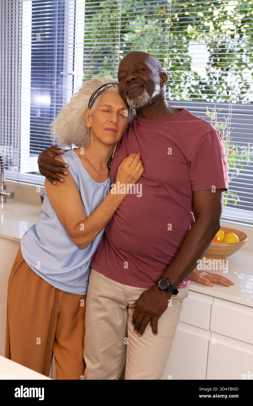 Abbracciando diverse coppie appoggiate insieme in una cucina luminosa, con ciotola di arance in legno Foto Stock