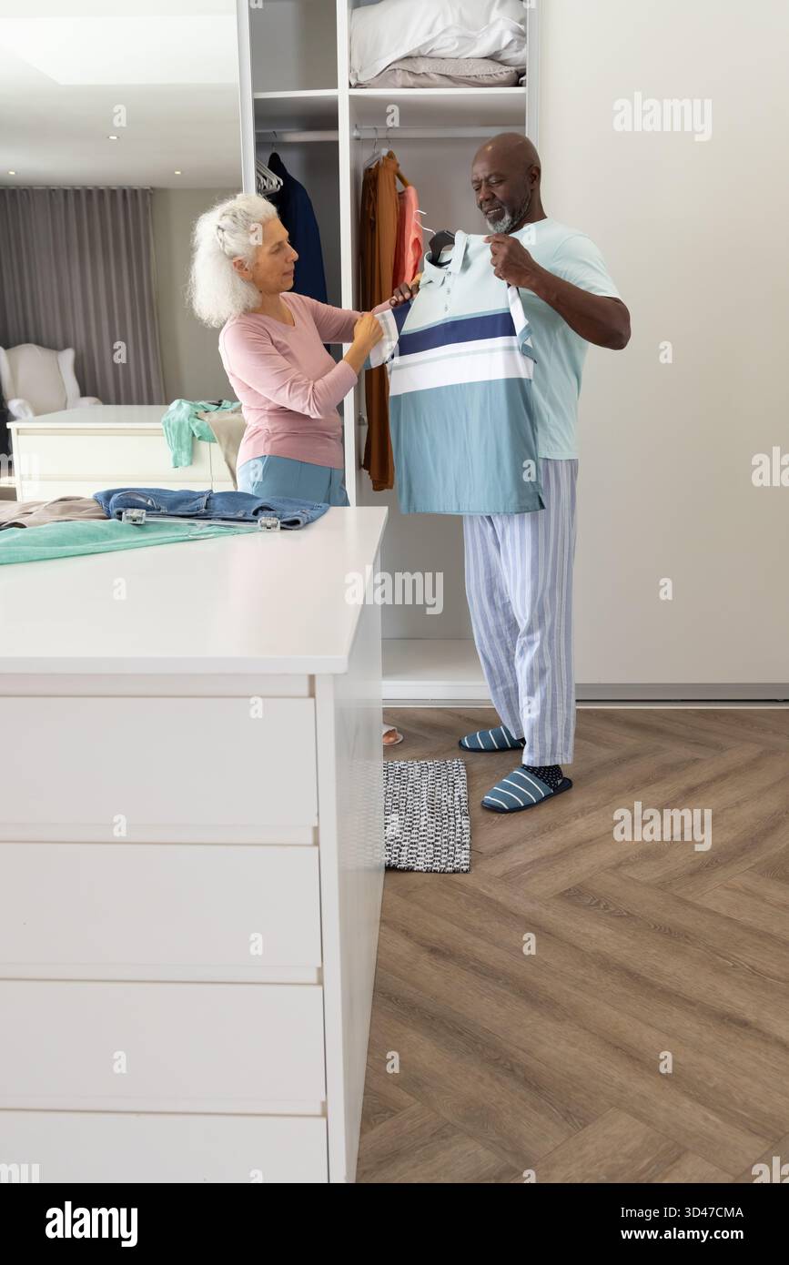 Una coppia senior sta esaminando una polo a righe nel moderno armadio grigio chiaro della camera da letto, spazio fotocopie Foto Stock