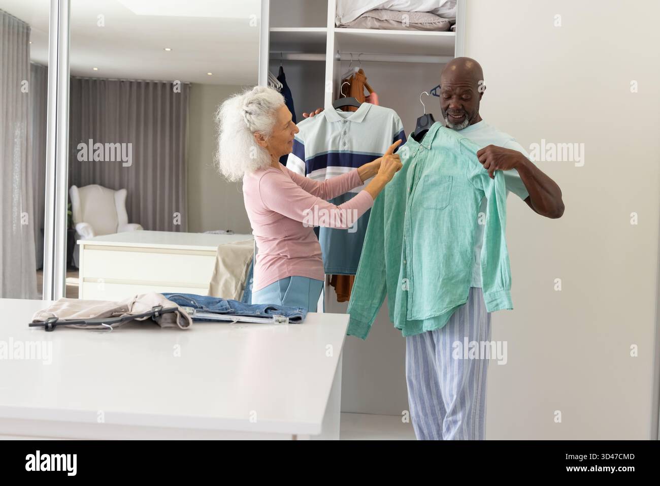 Confrontando le maglie selezionate da una coppia senior nello spogliatoio della casa, con polo a righe e camicia verde Foto Stock