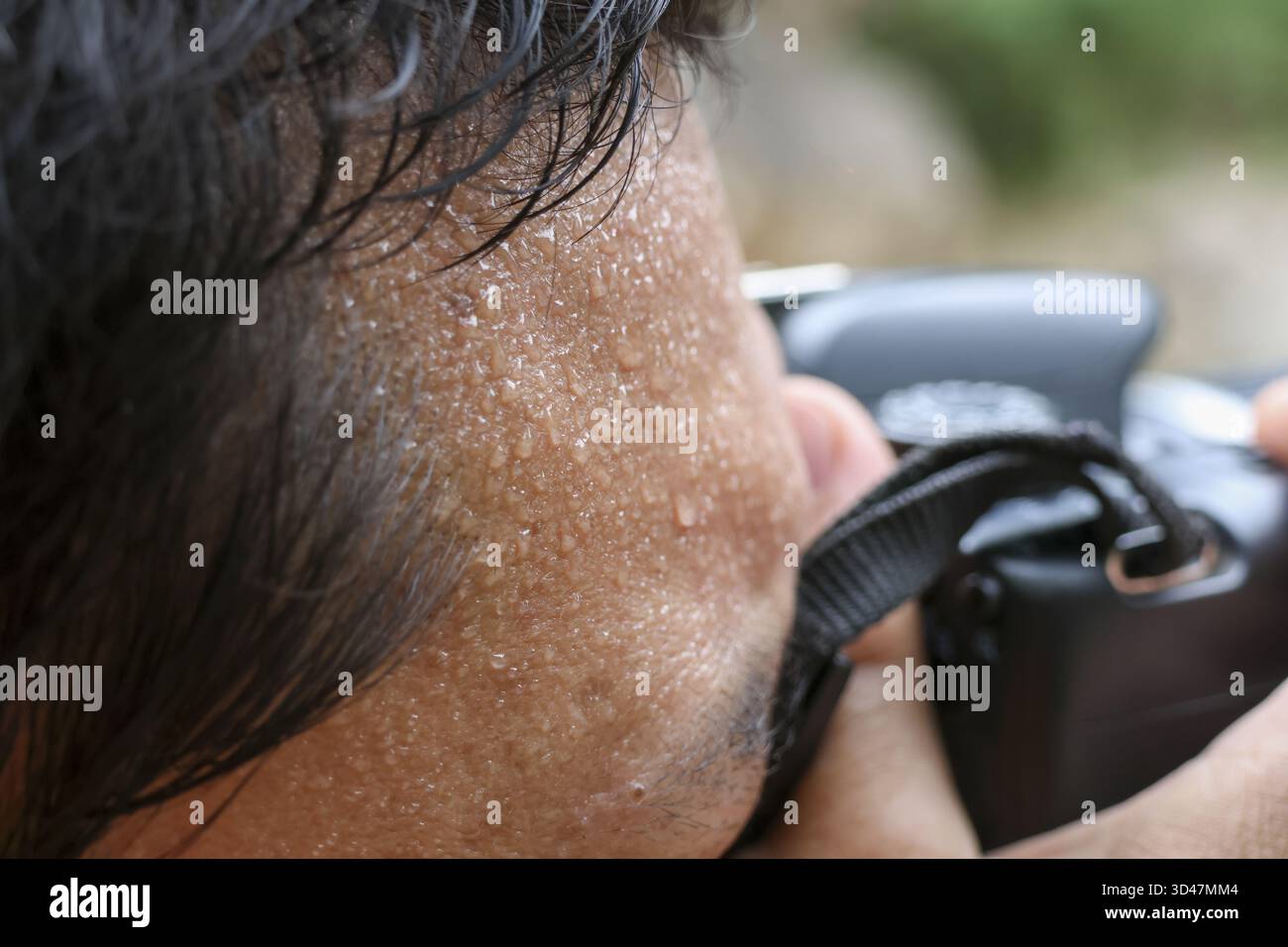 Uomo concentrato con sudore sul viso che scatta fotografie con la fotocamera all'aperto. il fotografo determinato si concentra sul suo soggetto in un ambiente caldo e umido Foto Stock