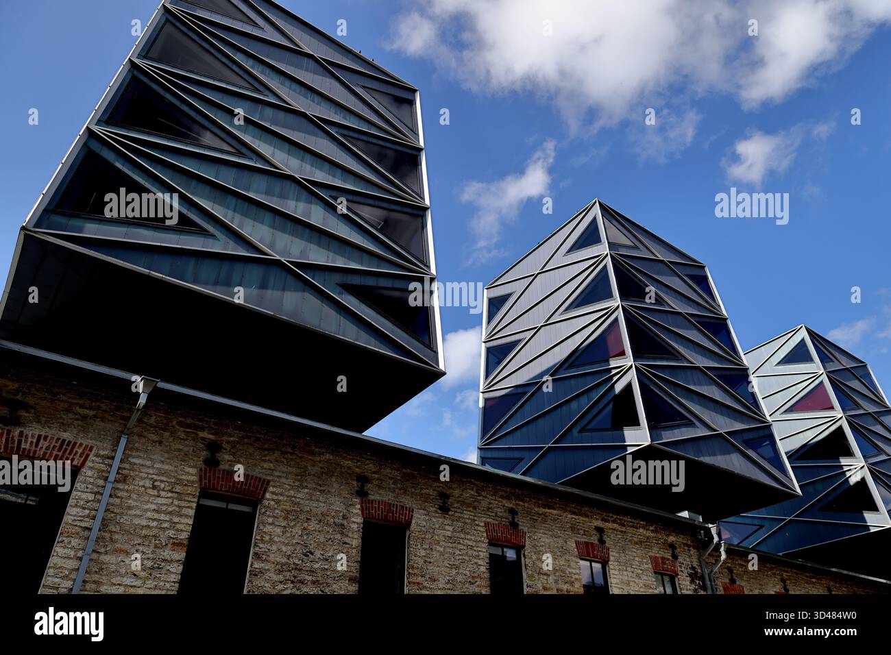 Volumi d'ufficio geometrici a sbalzo che si innalzano sopra una vecchia struttura in pietra sotto il cielo blu, fotografati a Vanalinn, Tallinn, Estonia, alla luce del giorno. Foto Stock