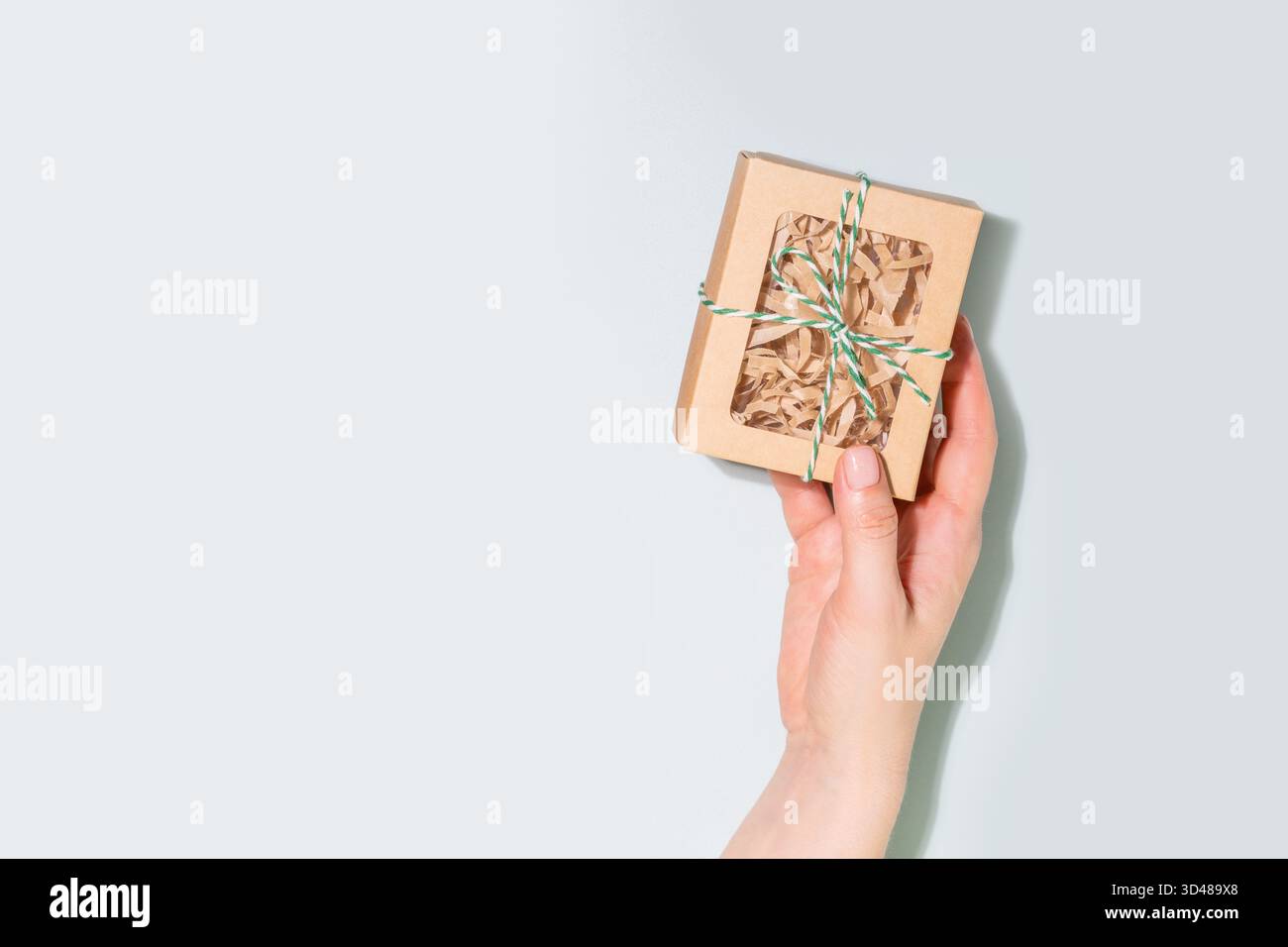 Confezione regalo di Natale a mano avvolta in carta artigianale con spago verde su sfondo blu. Concetto di pacchetti vacanza ecologici, regali consapevoli Foto Stock