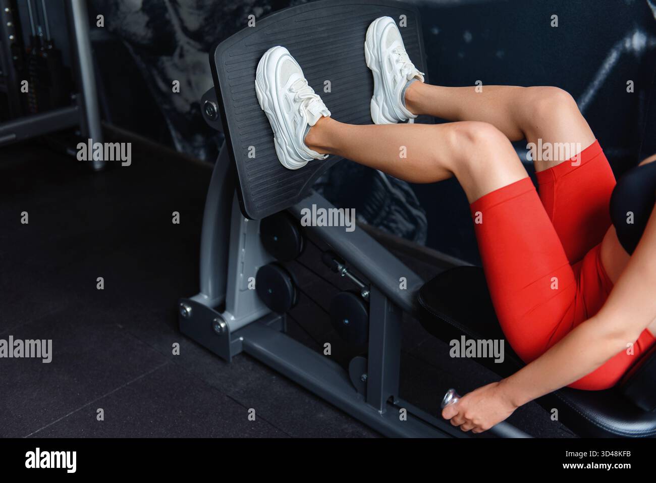 Giovane donna sportiva con reggiseno nero, pantaloncini rossi e zampe di allenamento bianche con simulatore di stampa. Allenamento femminile forte regolarmente al club sportivo clos Foto Stock