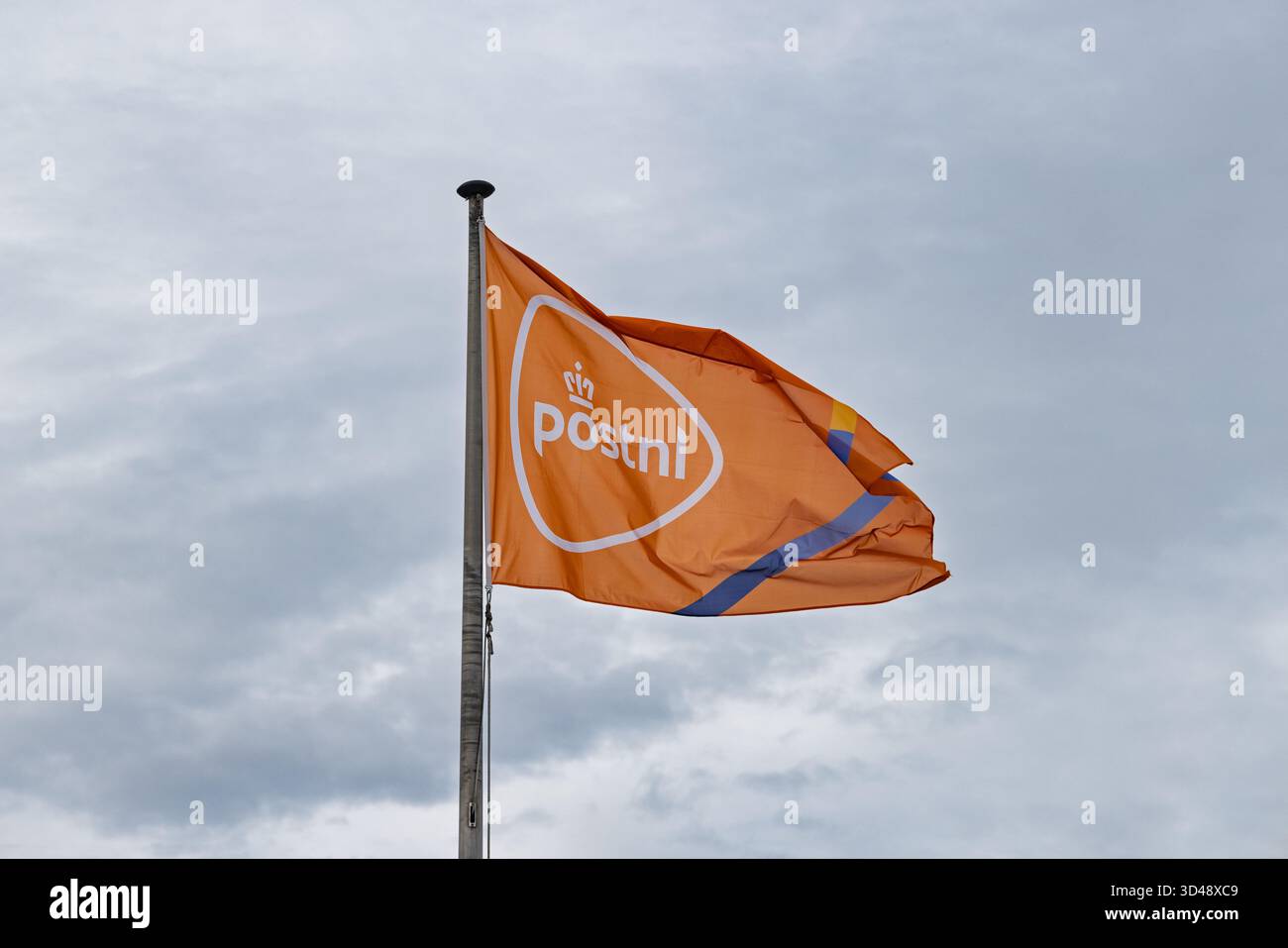 La bandiera arancione PostNL, con il suo logo a corona, soffia nel vento contro un cielo grigio nuvoloso. Utrecht Paesi Bassi, 31 ottobre 2025. Foto Stock