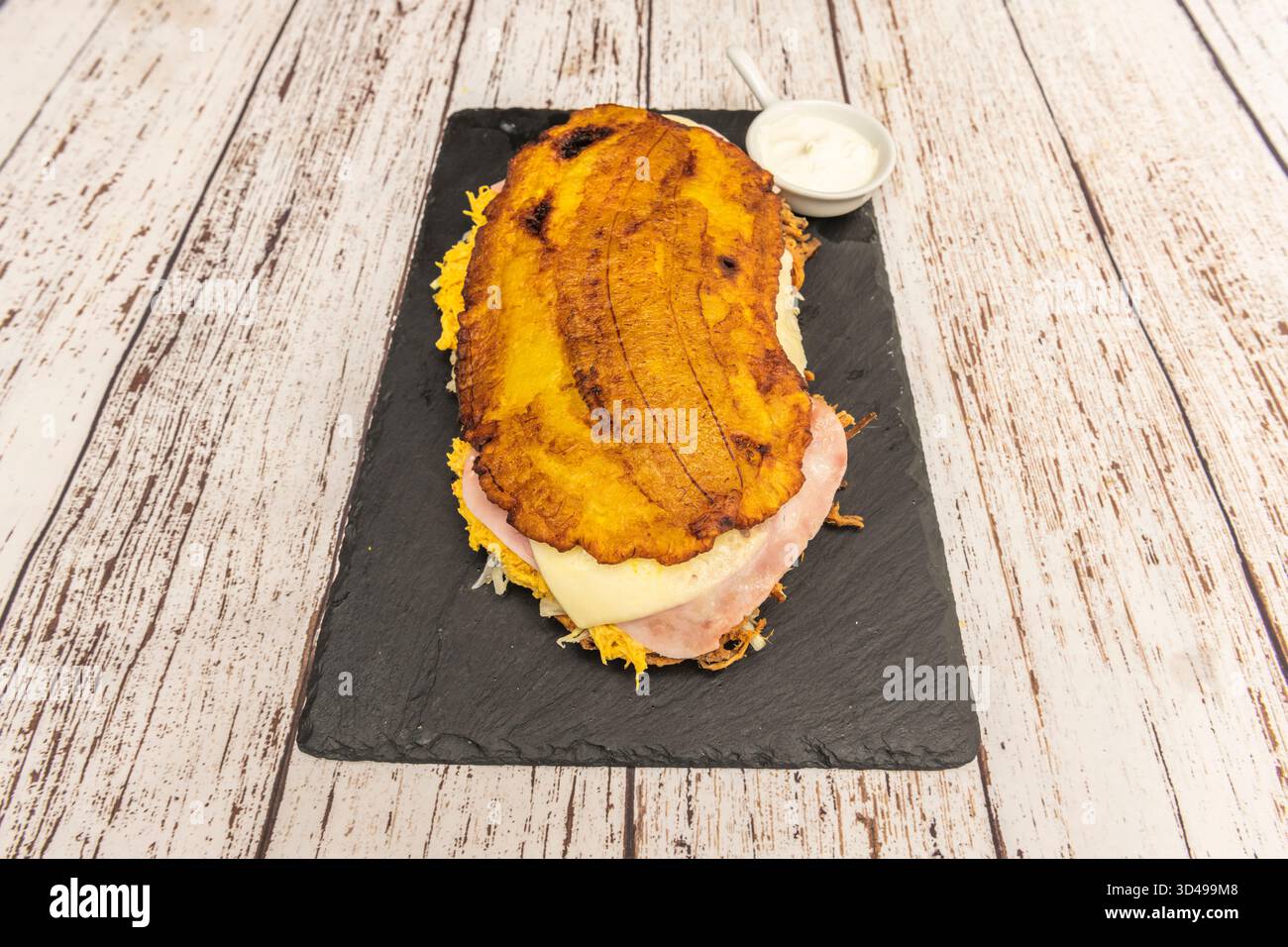 Pataconi tradizionali venezuelani, appiattiti e fritti due volte, conditi con strisce di queso de mano (un tipo di formaggio venezuelano) e serviti con siero di latte Foto Stock