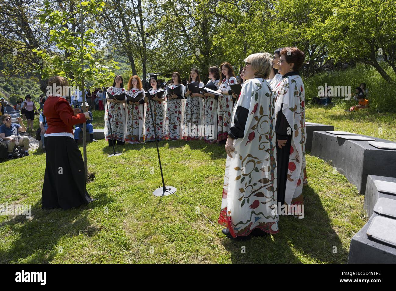 Coro femminile in abiti bianchi colorati che cantano all'aperto, circondato da alberi e pubblico, coro al monastero di Tatev, provincia di Syunik, Syunik, Armenia Foto Stock