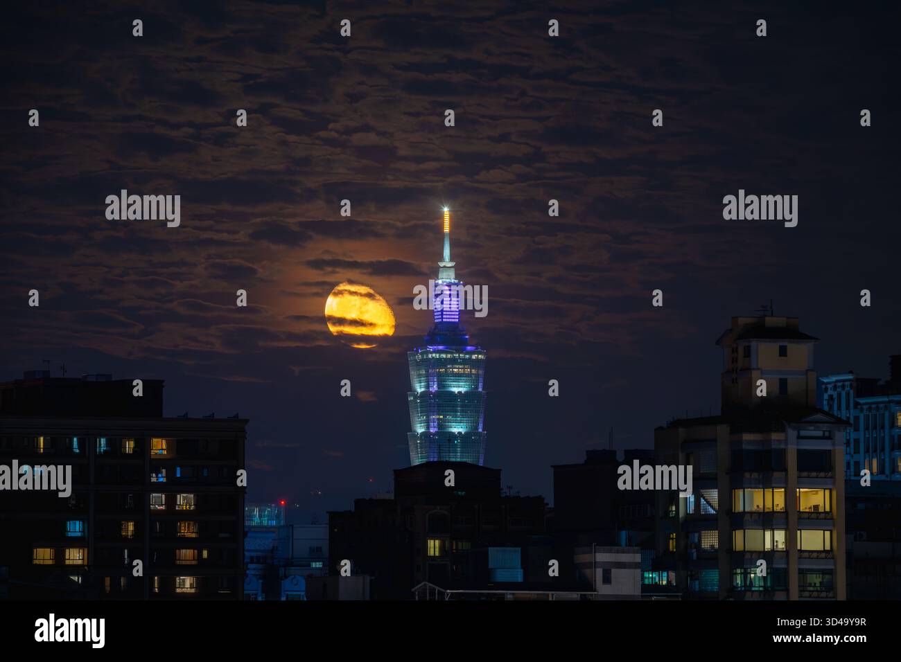 Sanchong, Taiwan - 15 giugno 2025: Una splendida scena notturna con la torre Taipei 101 illuminata con una luna crescente che si innalza dietro di essa. Illuminato Foto Stock