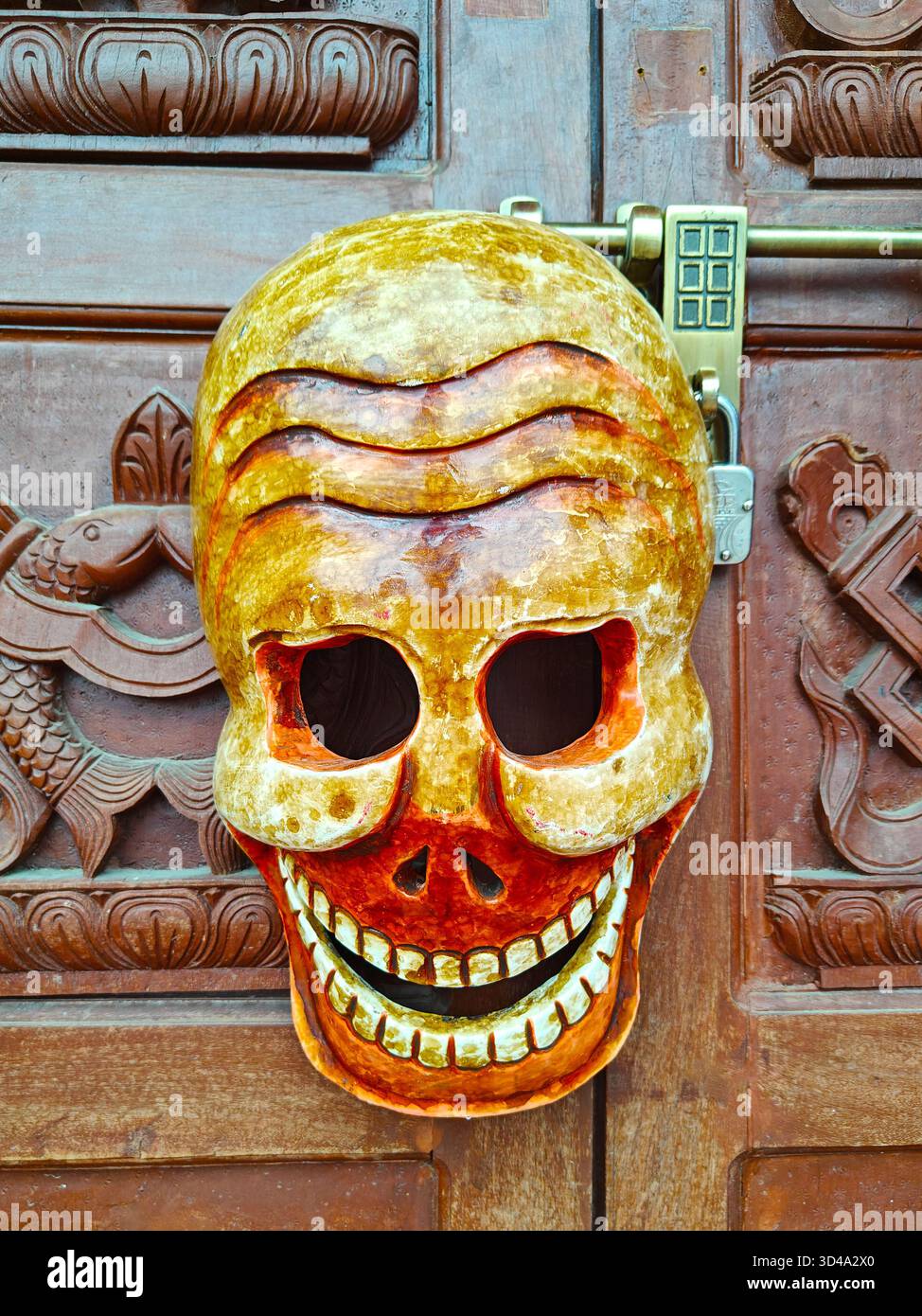 Vivace maschera cranica esposta su una porta in legno con intagli e lucchetto dettagliati Foto Stock