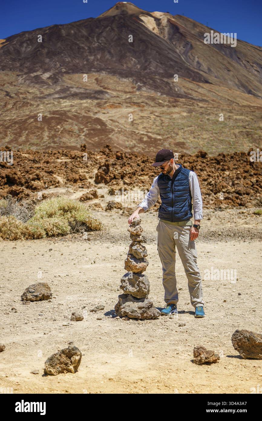 Un turista in un arido paesaggio roccioso con una montagna vulcanica Teide sullo sfondo, che costruisce un cairn per l'equilibrio o il concetto di avventura Foto Stock