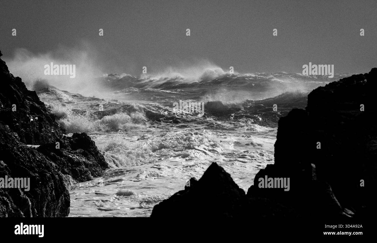 Mare turbolento con grandi onde a Kynance Cove sulla Penisola di Lizard, Cornovaglia. Incorniciata da rocce frastagliate. Immagine monocromatica. Foto Stock