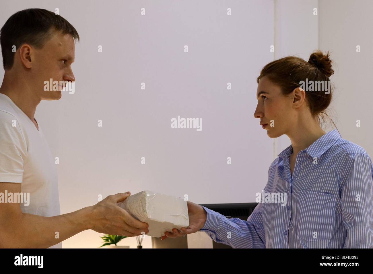 Consegna del pacco da parte del cliente al dipendente da un banco all'altro. Man estende il pacchetto confezionato a una donna dipendente che raggiunge il banco di vendita con monitor e impianto Foto Stock
