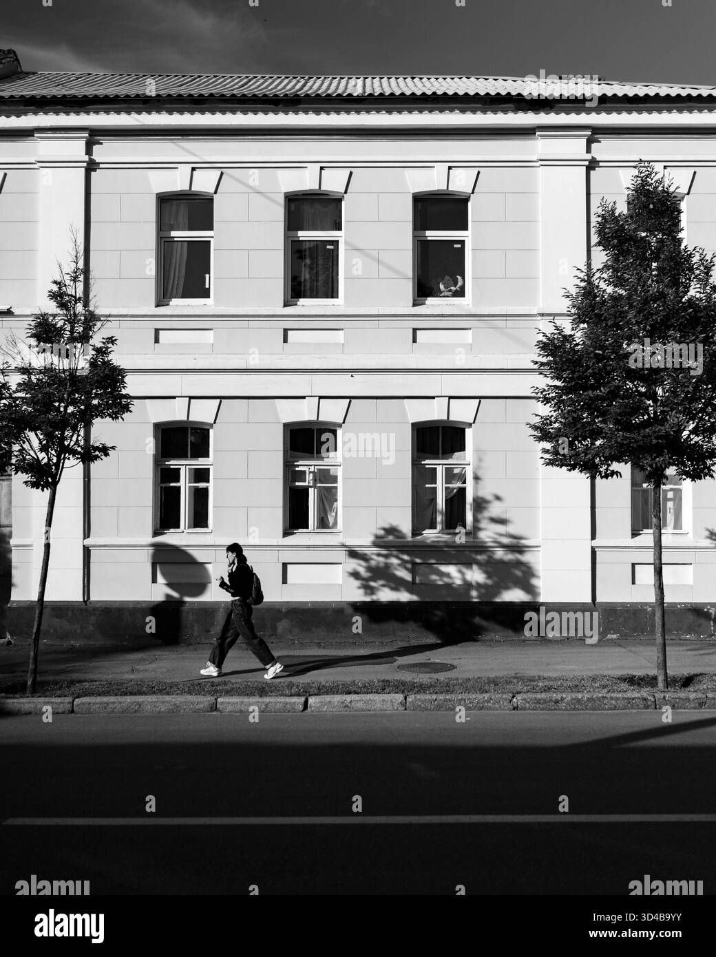 Scena urbana in bianco e nero con una persona che cammina lungo la facciata di un vecchio edificio. Il contrasto di luce e ombra enfatizza il ritmo architettonico e u Foto Stock