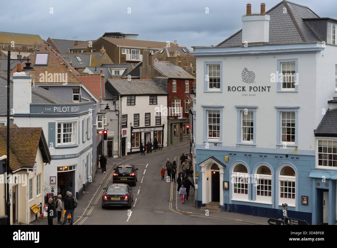 La gente passa accanto ai negozi e ai pub di Lyme Regis, Dorset, Regno Unito, vicino al porto di Cobb. Foto Stock