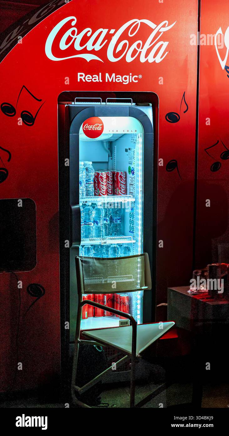 Frigorifero Red Coca-Cola con bevande e bottiglie d'acqua illuminate in un ambiente buio. Coca-Cola come marchio essenziale per il rinfresco e coinvolgente Foto Stock