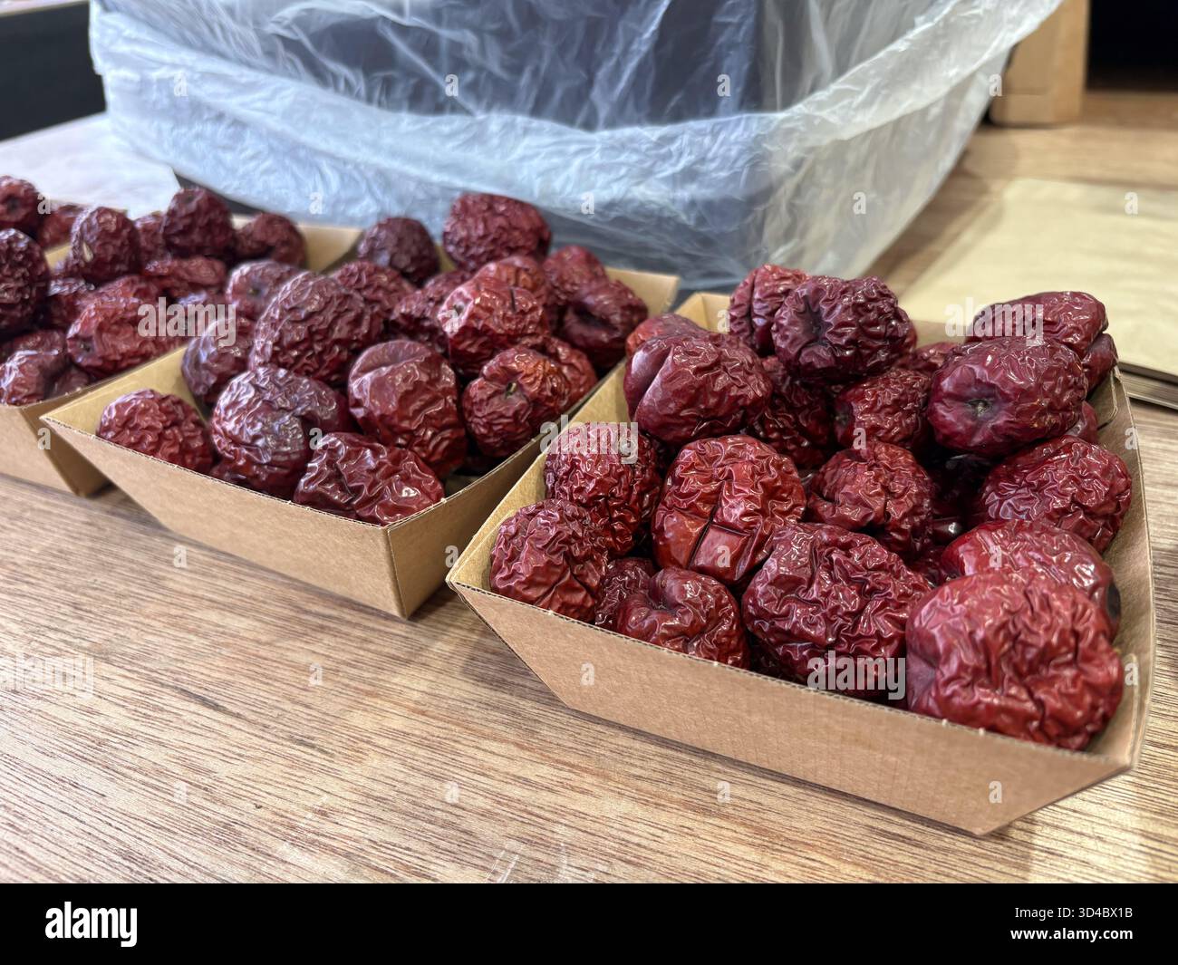 Datteri rossi giuggiati secchi, noti anche come datteri cinesi, esposti in piccoli vassoi di cartone su una superficie di legno, pronti per la vendita o il consumo. Foto Stock