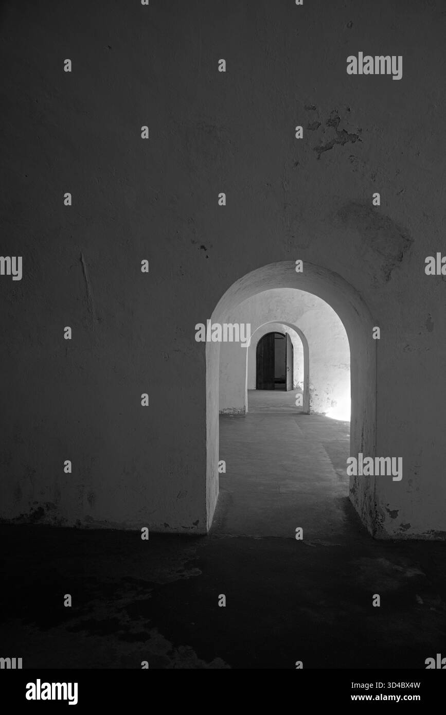 Una serie di arcate crea un effetto tunnel in uno spazio minimalista e poco illuminato. Ombre e luci giocano sulla superficie ruvida delle pareti. Foto Stock