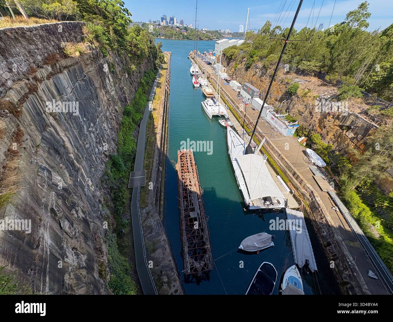 La vista panoramica di Woolwich Lookout mostra le barche attraccate in uno stretto corso d'acqua lungo ripide pareti rocciose, con un lontano skyline di Sydney sotto cieli limpidi. Parte della LAN Foto Stock