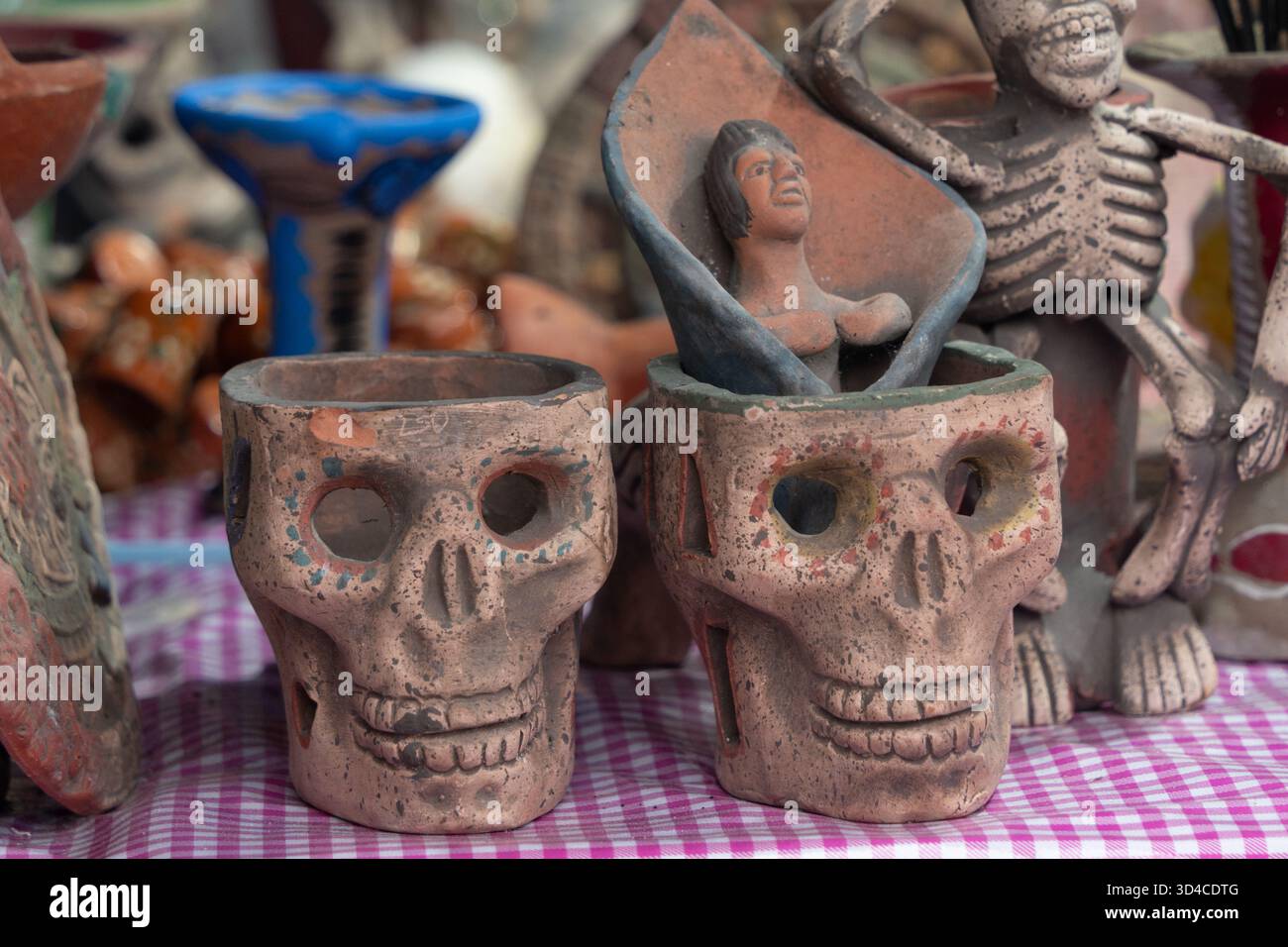 Due teschi sono seduti su un tavolo accanto a uno scheletro. I teschi sono decorati con denti. La tradizione messicana del giorno dei morti, offerte, cibo, colori, Foto Stock