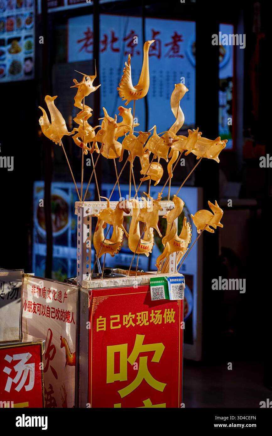 Bancarello di strada che vende la tradizionale arte dello zucchero ludao di Pechino vecchia, un dolce piatto cinese locale fatto di sculture di malto soffiate a forma di animale Foto Stock