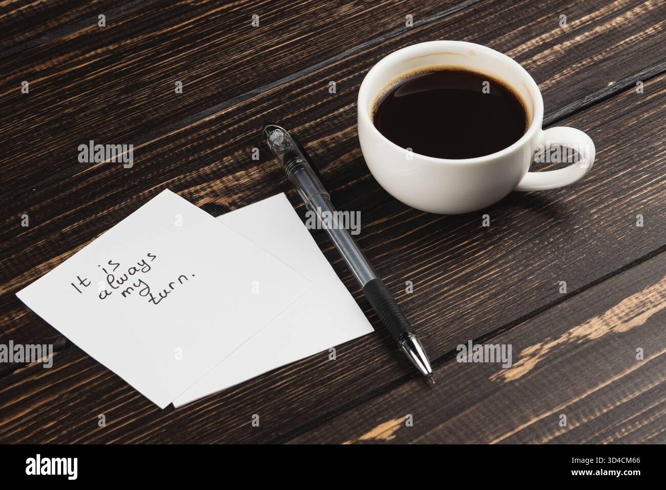 Una tazza di caffè bianca si appoggia accanto a una nota scritta a mano su un tavolo di legno, trasmettendo un messaggio personale sull'attesa di un turno. La scena sembra accogliente e. Foto Stock