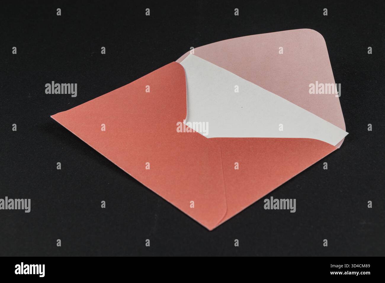 Una busta aperta mostra un esterno vibrante in corallo e una morbida fodera bianca. Lo sfondo scuro evidenzia i colori e le texture della busta Foto Stock