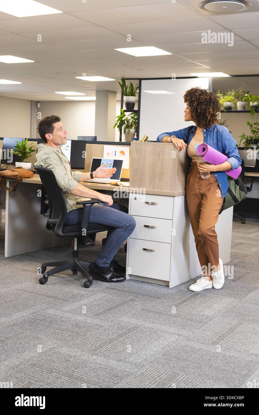 Diversi colleghi discutono i dettagli del progetto in un ufficio open space, con tappetino per yoga e bottiglia d'acqua Foto Stock