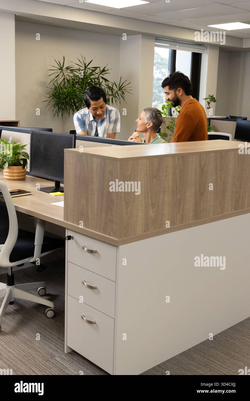 Collaborazione con colleghi diversi che condividono idee alla scrivania open space, con due monitor Foto Stock