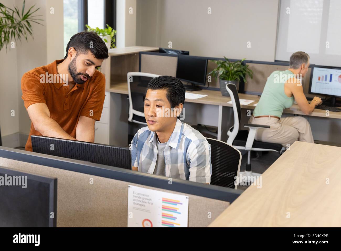 Collaborazione con diversi colleghi di lavoro che si appoggiano alle scrivanie in un ufficio open space, con monitor per computer Foto Stock