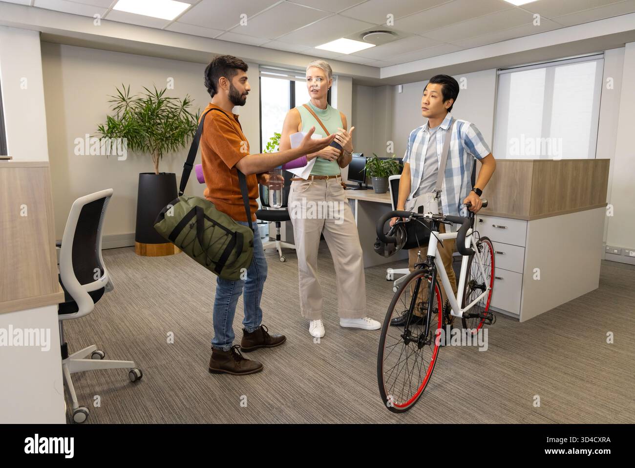 Parlare di colleghi diversi in un ufficio open space, con borsone verde e bicicletta da strada Foto Stock