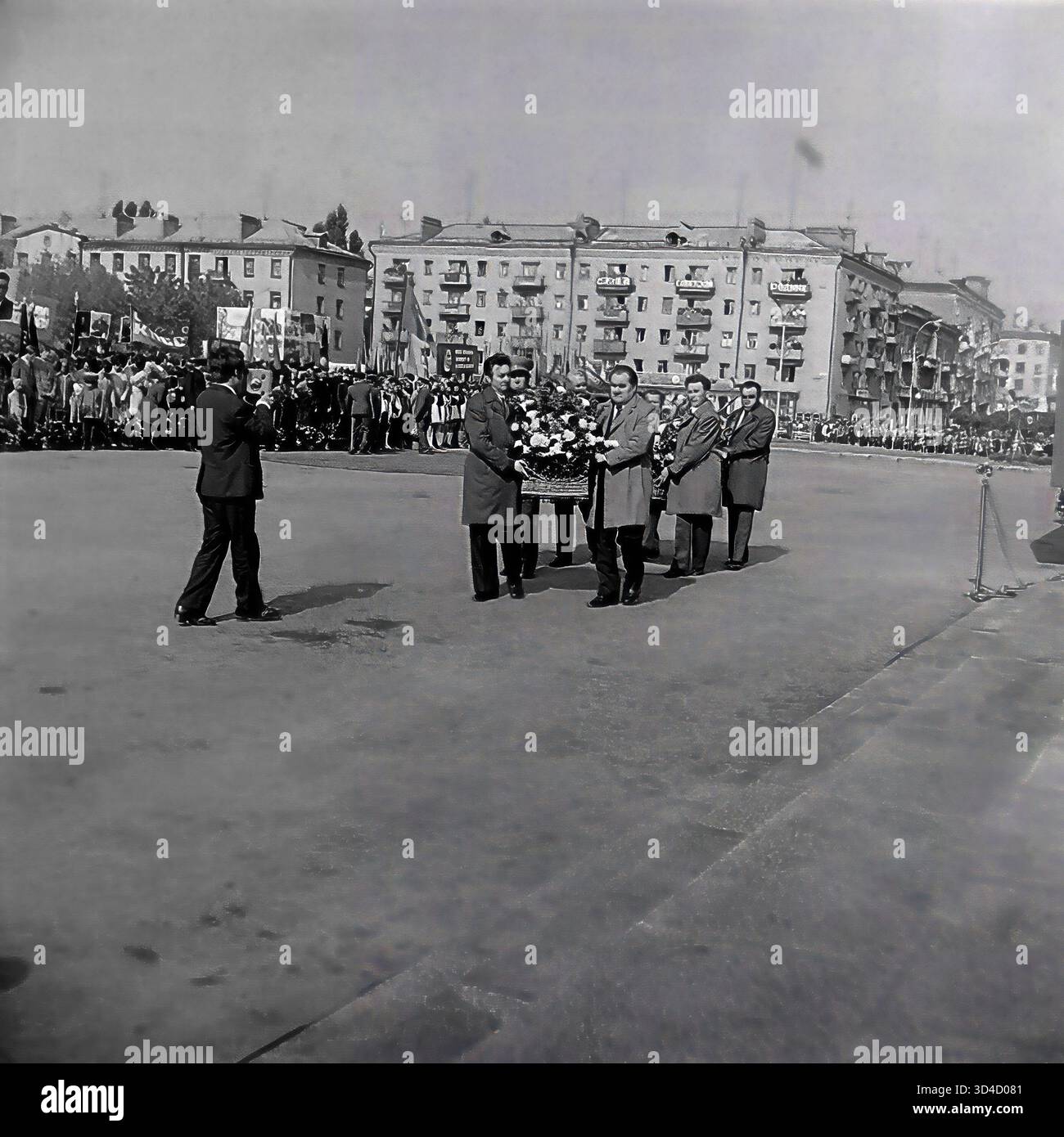 Una foto d'archivio degli anni '1980 cattura la celebrazione del 7 novembre (anniversario della Rivoluzione d'ottobre) a Sloviansk, RSS Ucraina. Una delegazione di uomini (funzionari della città) porta una grande corona attraverso la Piazza della Rivoluzione d'ottobre (ora Piazza Soborna) per giacere al monumento di Lenin. Un fotografo scatta la propria foto, mentre la folla di manifestanti con le bandiere fiancheggiano la piazza. Questo cattura una festa politica ufficiale sovietica. Questo è un momento di vita pubblica nel pacifico Donbas prima della guerra. Foto Stock