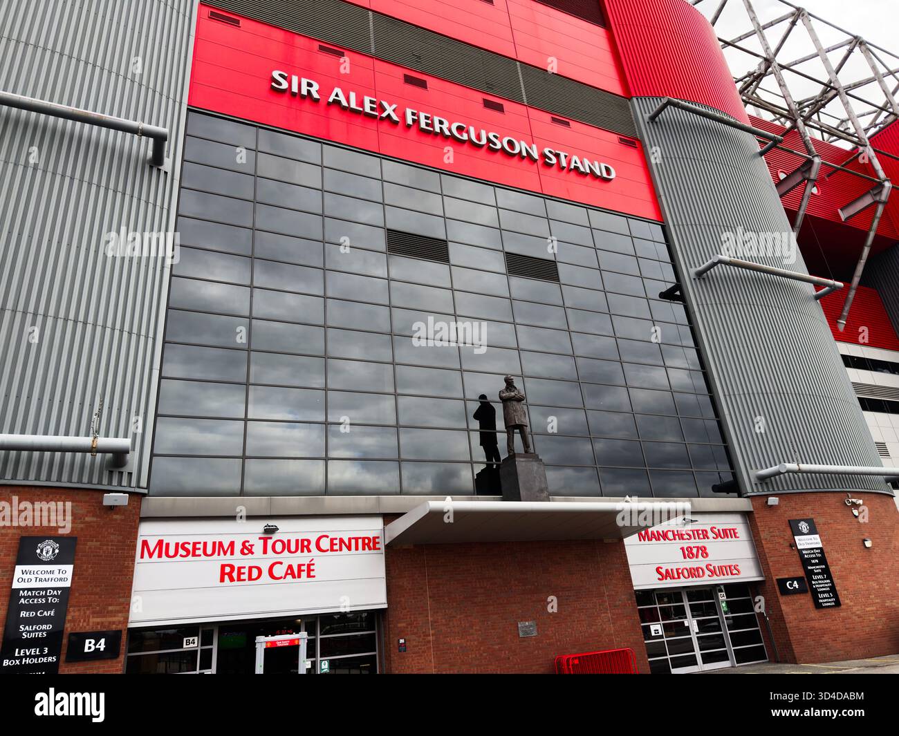 Manchester, Regno Unito - 30 settembre 2025: Facciata rossa e grigia dello stadio con parete di vetro, statua e ingresso al caffè del museo di Manchester Foto Stock