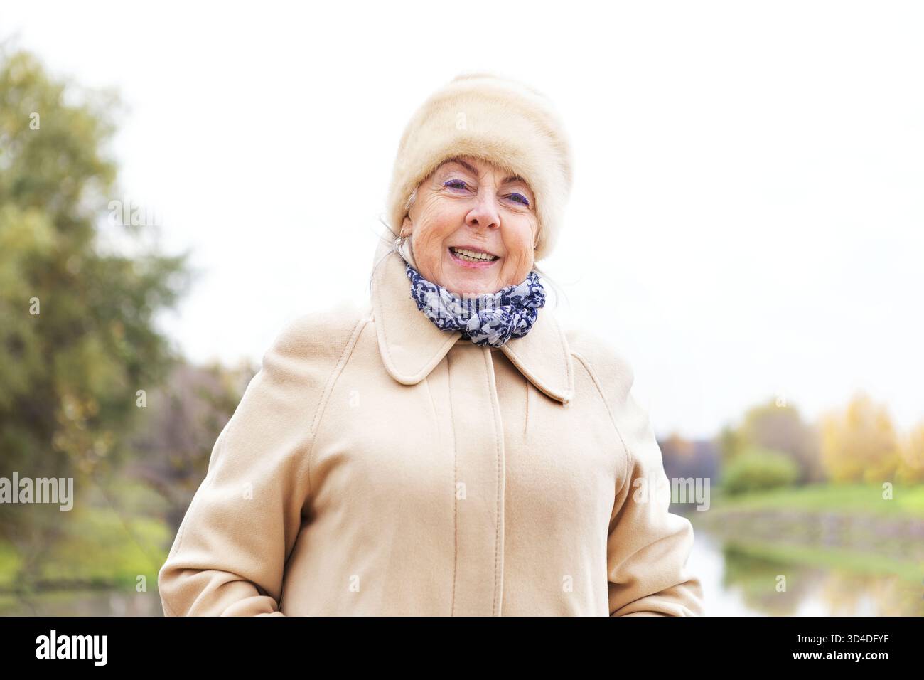 Donna anziana felice con cappotto caldo e cappello di pelliccia in un giorno d'autunno. Donna d'affari caucasica sorridente. Ritratto femminile in pensione per la pubblicità. Foto Stock