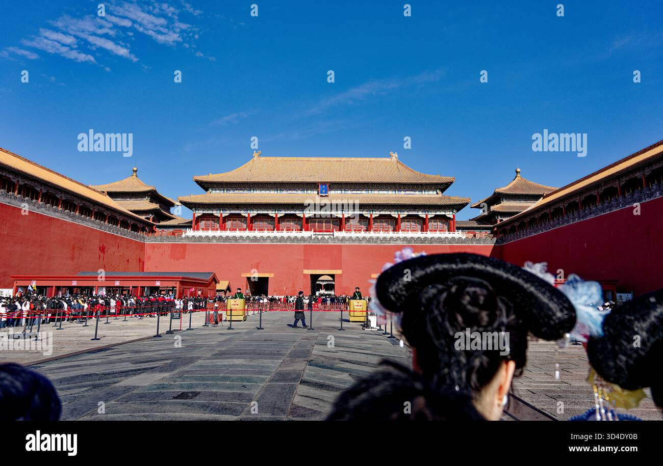 Code alla città Proibita, Pechino, simmetria del palazzo sotto il cielo blu con i visitatori in acconciatura tradizionale in primo piano Foto Stock