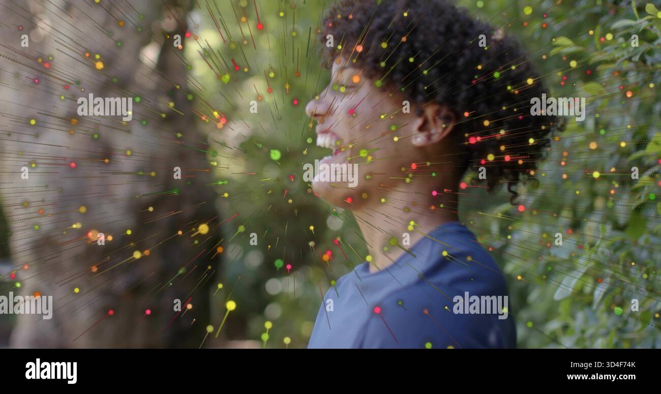 Uomo sorridente che indossa una t-shirt blu in piedi in giardino, con orecchini e rivestimento multicolore Foto Stock