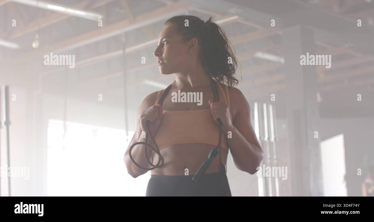 Regge manici con corda nera, donna che si allena in magazzino, indossa reggiseno sportivo abbronzato, leggings scuri Foto Stock