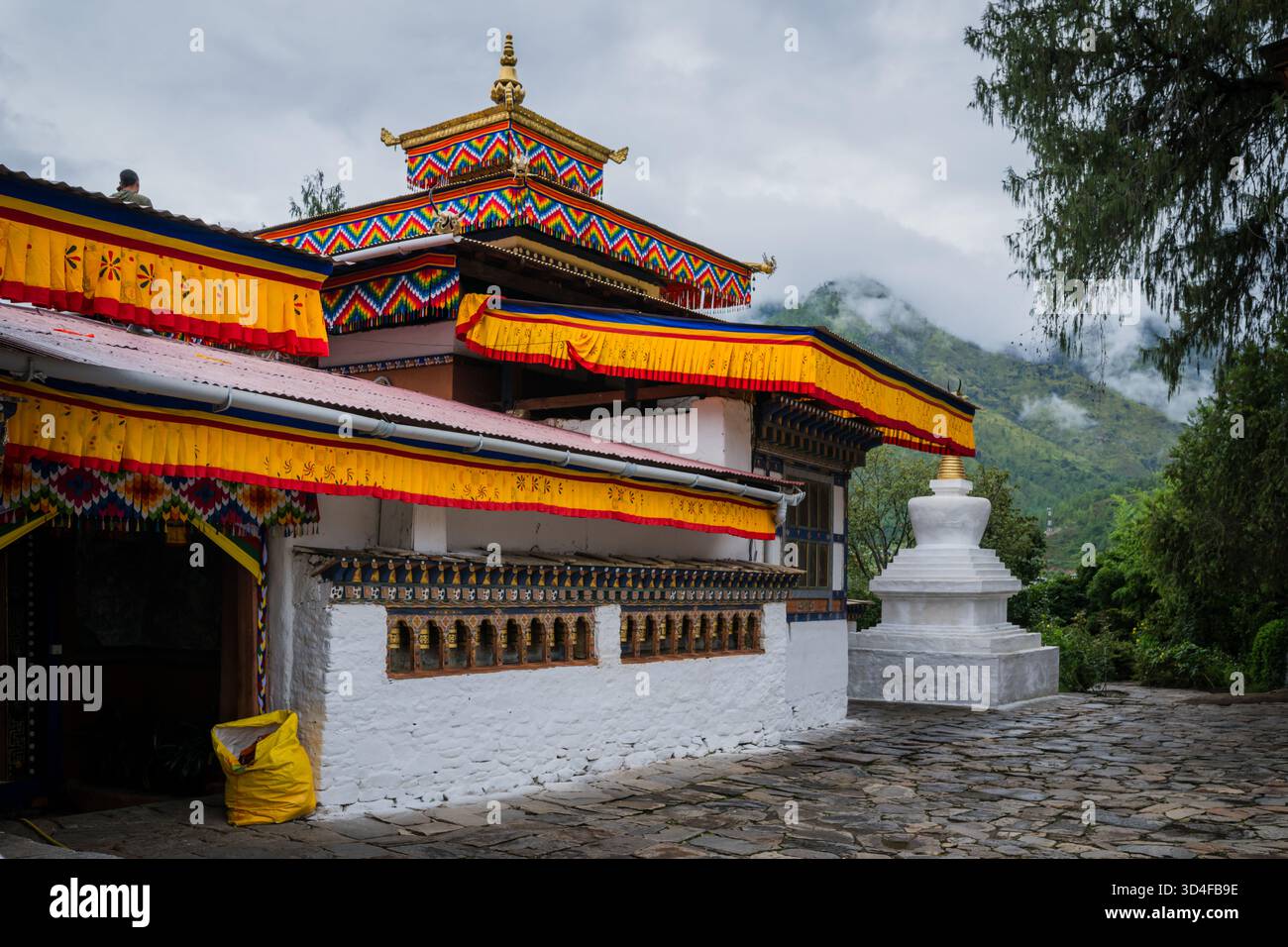La vista del tempio bhutanese con tetti dorati e tende gialle si erge maestosamente su uno sfondo di montagne nebbiose, Paro, Bhutan. Foto Stock