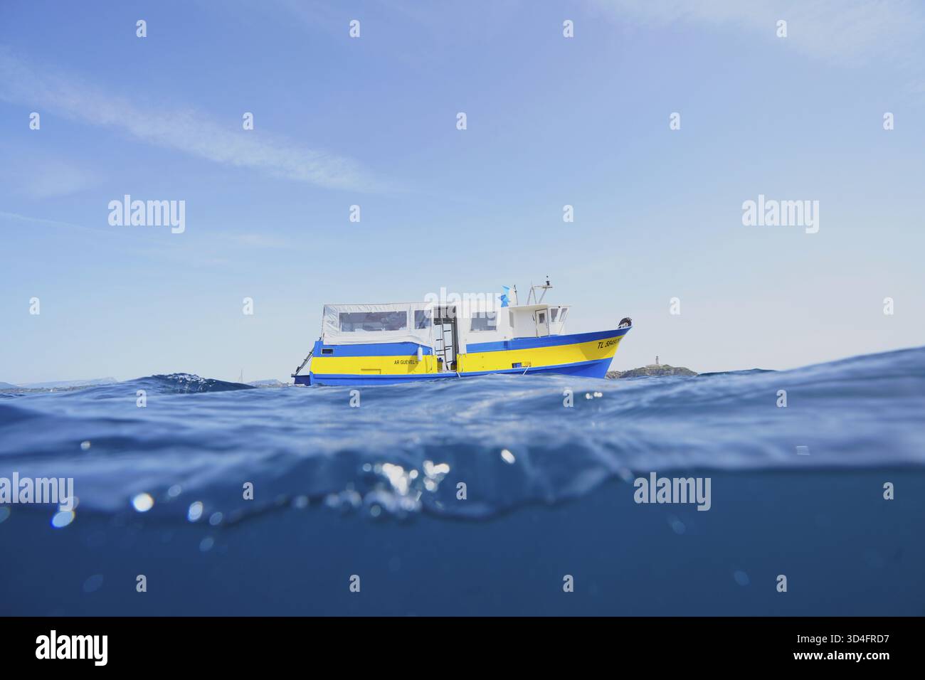 Una barca giallo-blu, una nave a motore, una barca per immersioni galleggia sul mare calmo sotto un cielo limpido sul Mar Mediterraneo vicino a Hyeres, penisola di Giens Foto Stock