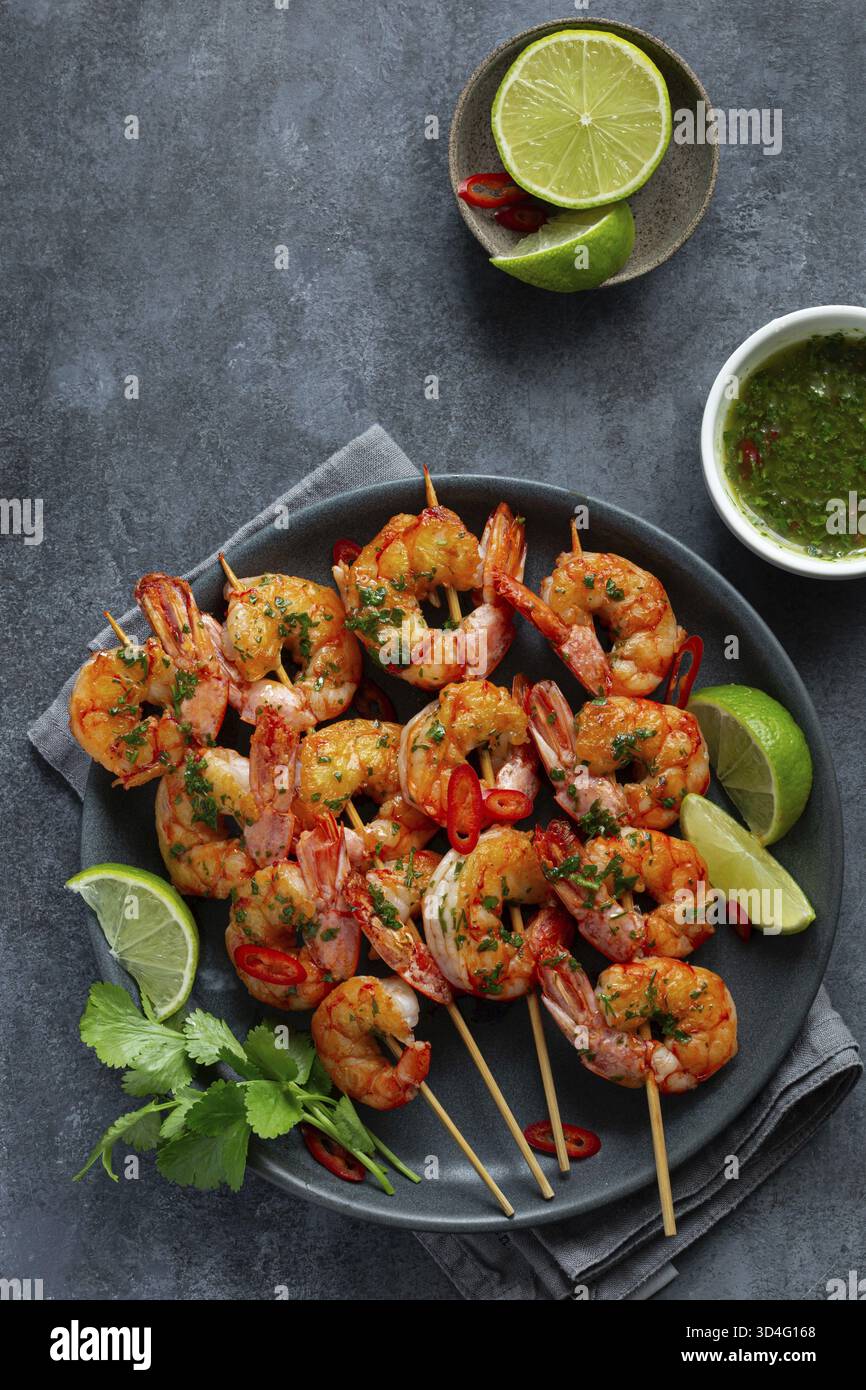 Cibo, spiedini di gamberi alla griglia con salsa chimichurri verde, vista dall'alto, sfondo scuro Foto Stock