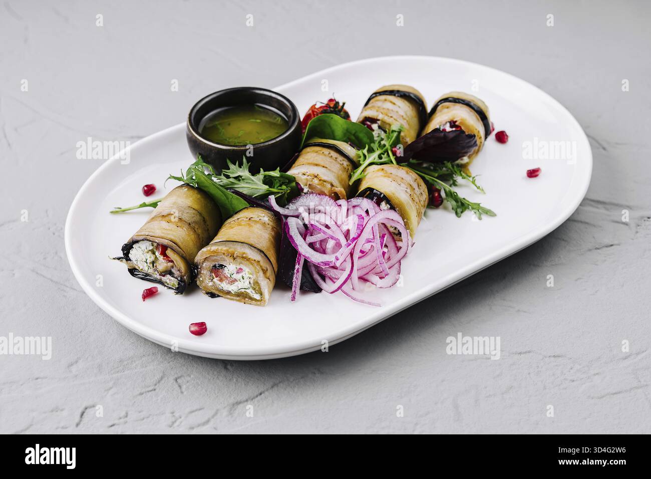 Cibo, involtini di melanzane delicatamente placcati con un lato di salsa salata e guarnigioni fresche Foto Stock